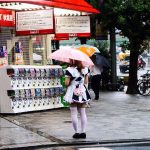 Woman in a maid costume holding a pink umbrella beside capsule-toy machines in Akihabara