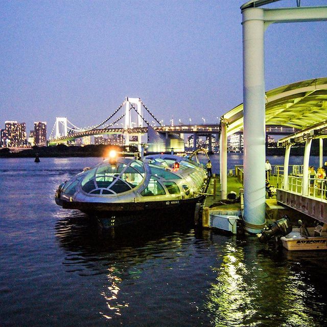 River Cruise on Sumida River in Tokyo Japan Tokyo Cruise boat moored beside a waterfront pier with Rainbow Bridge illuminated behind it