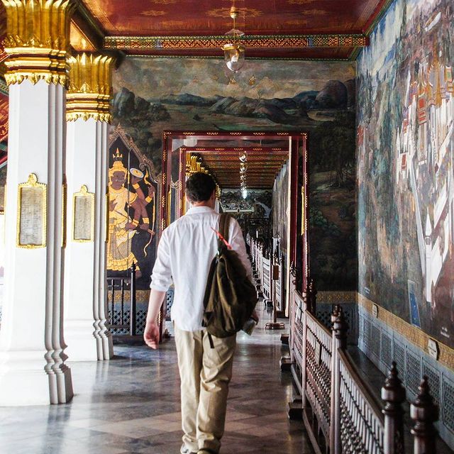husband walking past mural in temple in bangkok thailand