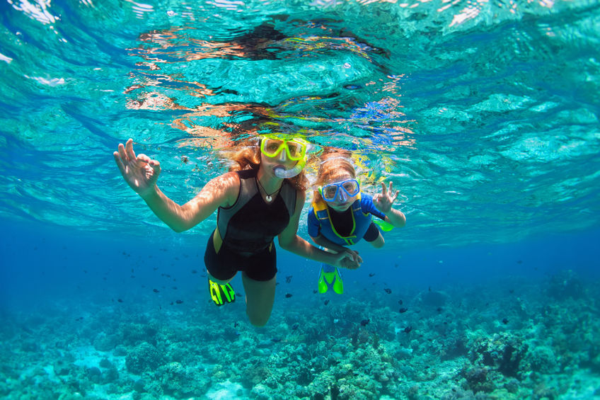mother and kid in snorkeling mask dive underwater with tropical fishes in coral reef sea pool in krabi