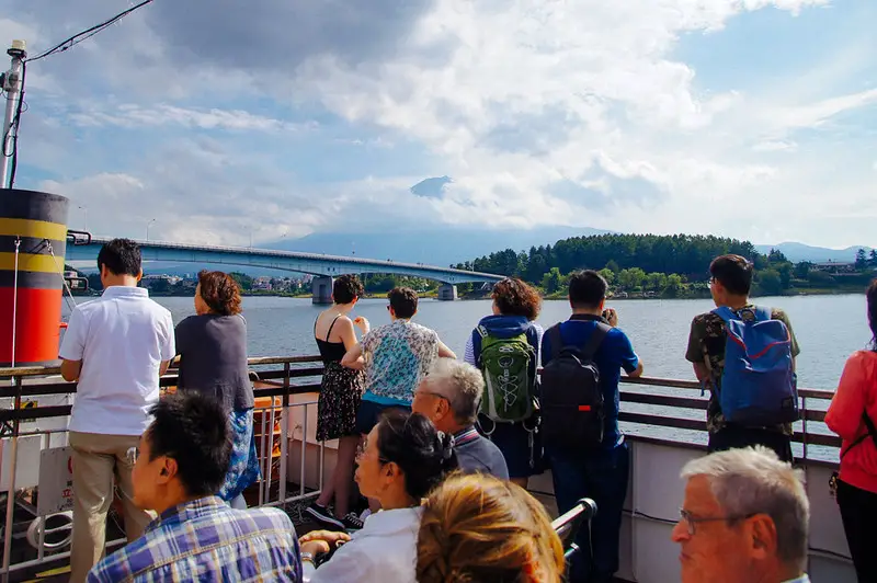 tourists on sightseeing boat on lake kawaguchiko with mountains in background