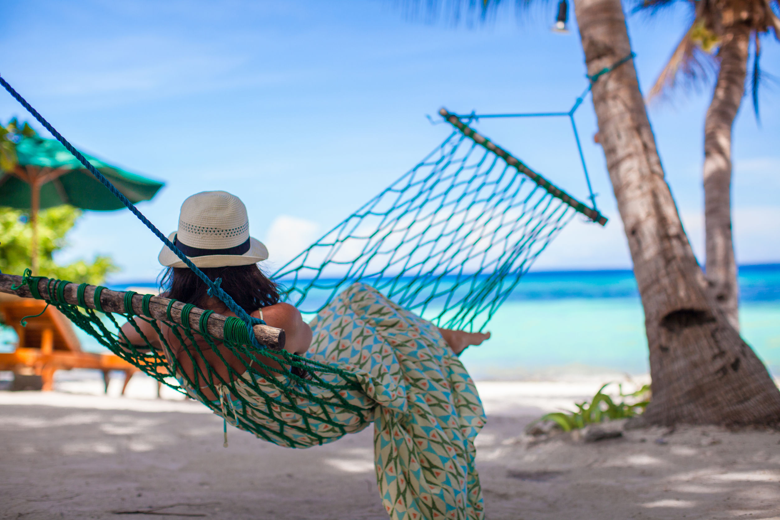 Woman in a sunhat relaxing in a hammock beside a tropical beach