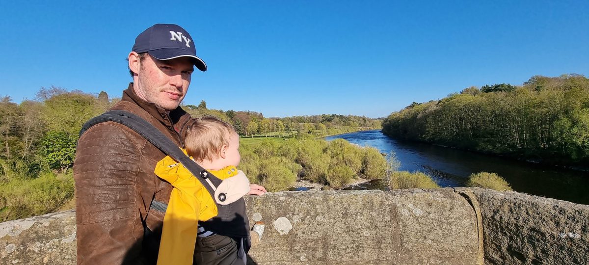 Travelling Abroad With A Baby at the riverside Dad travelling abroad with a baby standing on a bridge over a river