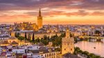 A panoramic sunset view of Seville, Spain, featuring the illuminated La Giralda bell tower, the Cathedral, and the Torre del Oro on the banks of the Guadalquivir River.