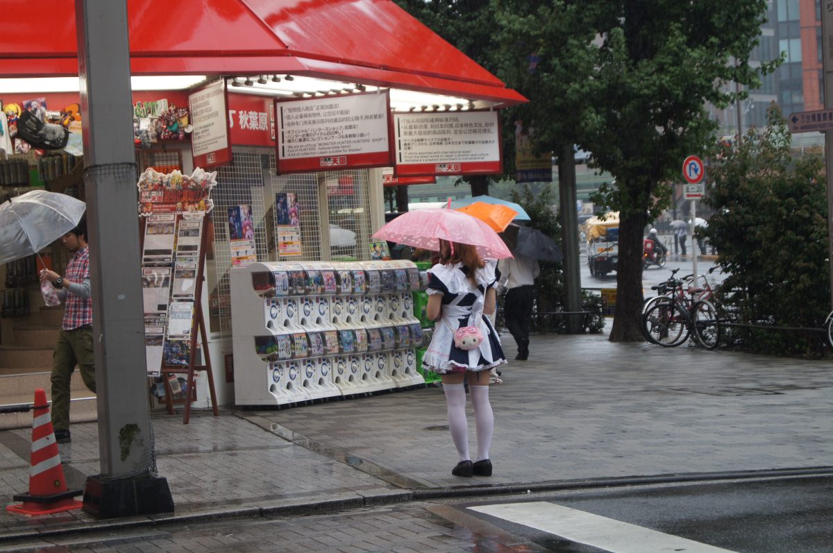 Akihabara 6 A maid with a pink umbrella near capsule-toy machines on a rainy Akihabara street