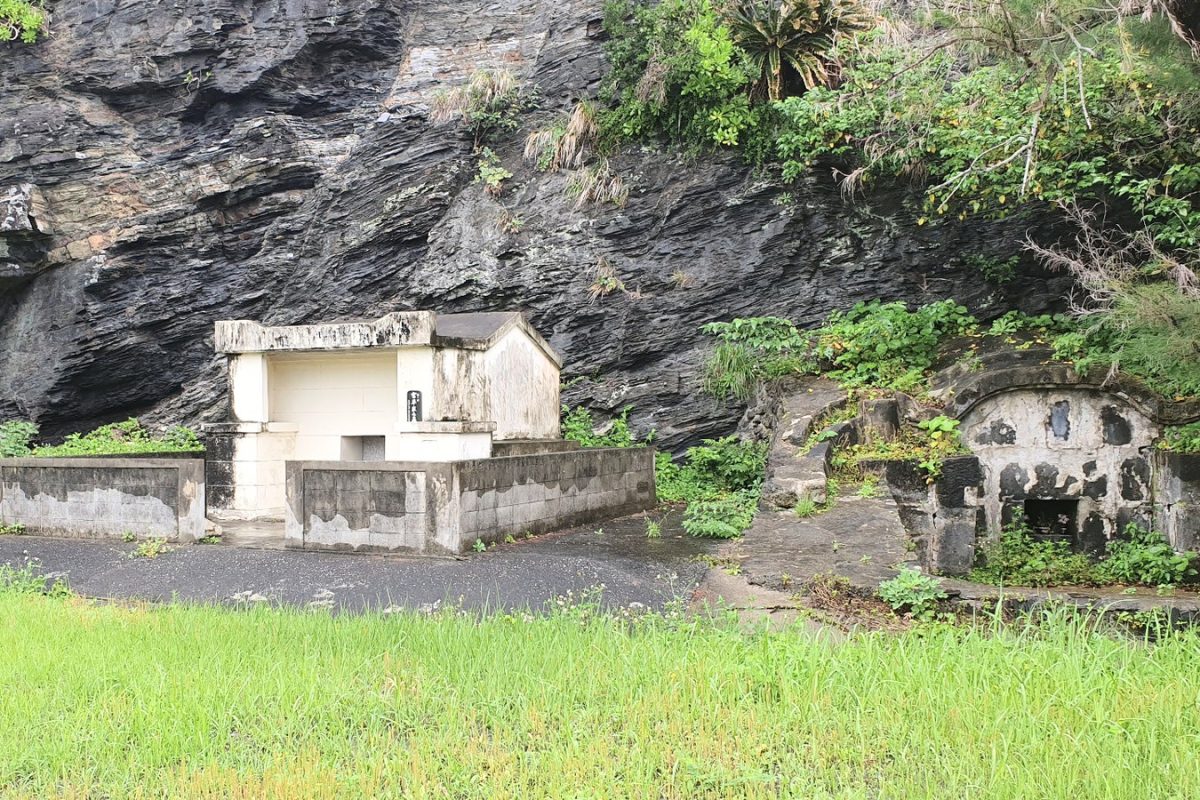 Traditional tombs beneath a rocky cliff, surrounded by grass and greenery on Zamami.