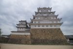 Himeji Castle keep rising above its stone base under a grey sky