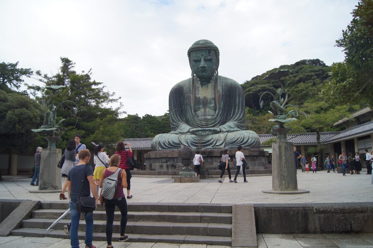 Visitors stand on the steps and courtyard in front of the seated Great Buddha at Kotoku-in.