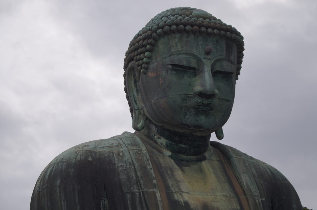 A close view of the calm bronze face of the Great Buddha of Kamakura against a cloudy sky.