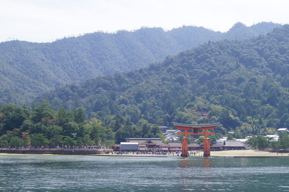 DSC06257 The great torii stands offshore against the wooded mountains and shoreline of Miyajima.