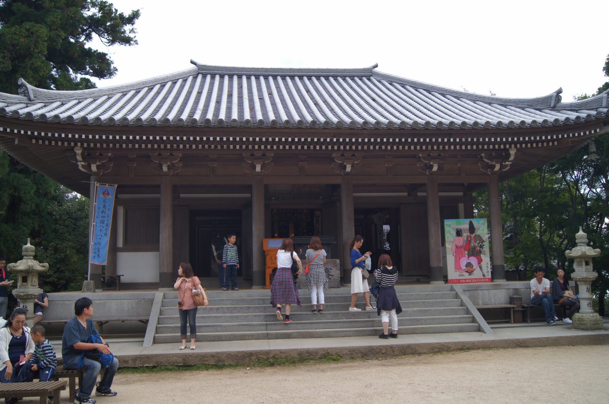 DSC06336 Visitors stand on the steps of a broad wooden temple hall at Daishō-in Temple on Miyajima, Japan.