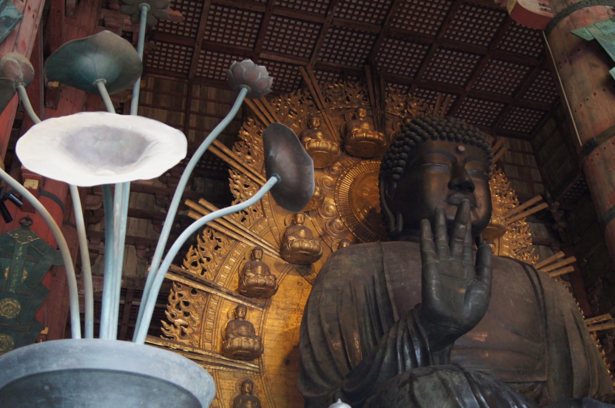 The Great Buddha and golden halo framed by bronze lotus lamps inside Tōdai-ji, Nara.