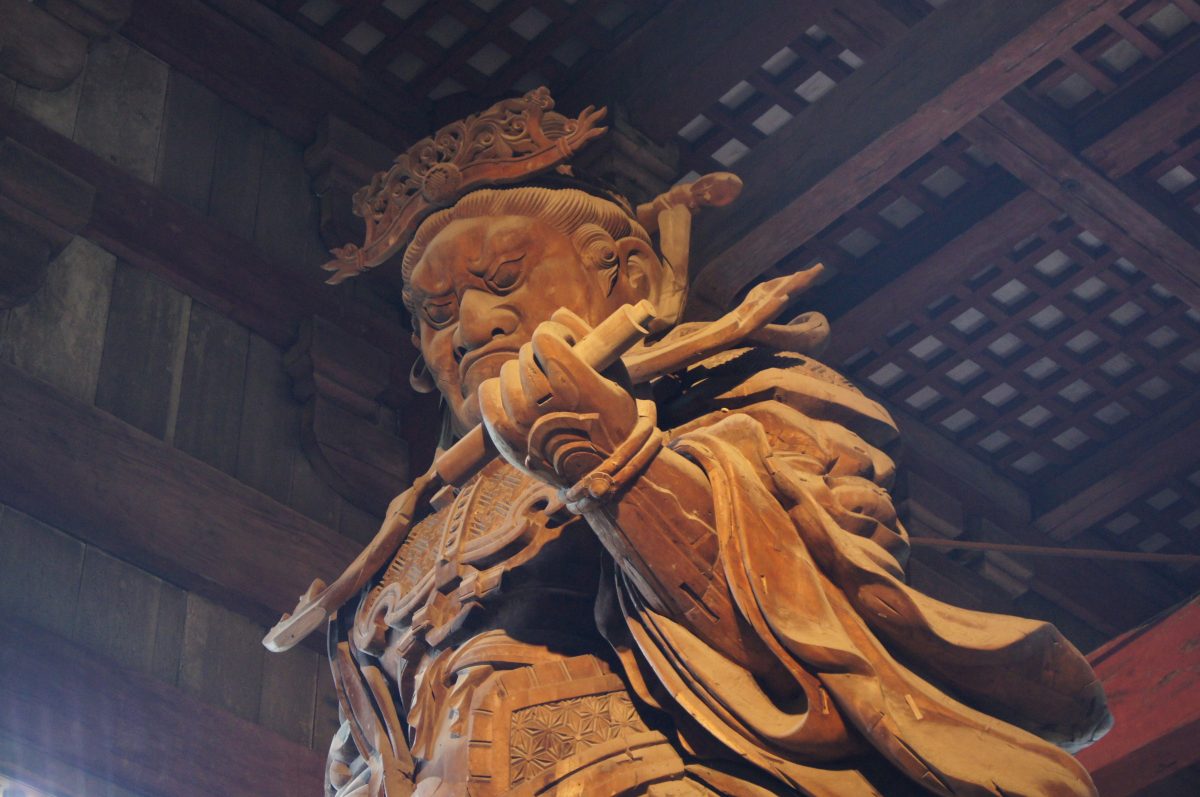 Close-up of a wooden guardian deity statue beneath the timber roof of Tōdai-ji’s Great Buddha Hall.