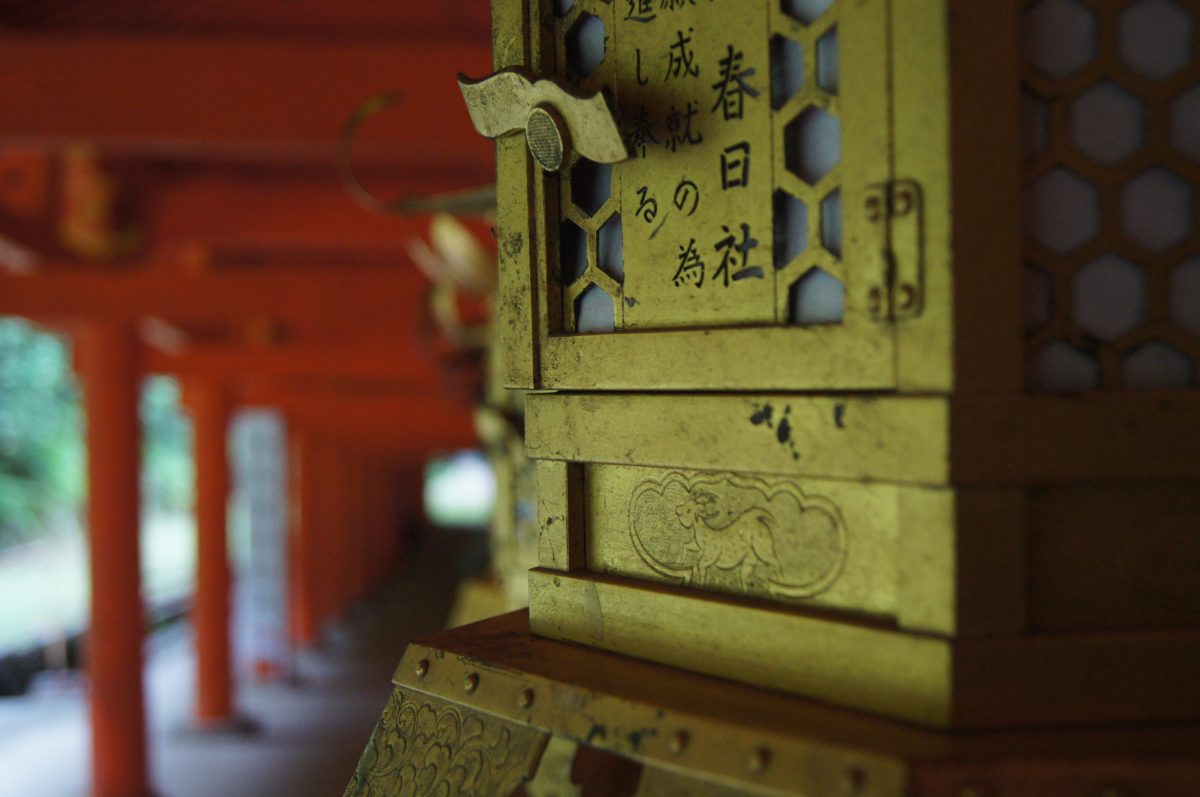 Close-up of a Japanese lantern with calligraphy inside a vermilion corridor at Kasuga Taisha Shrine in Nara.