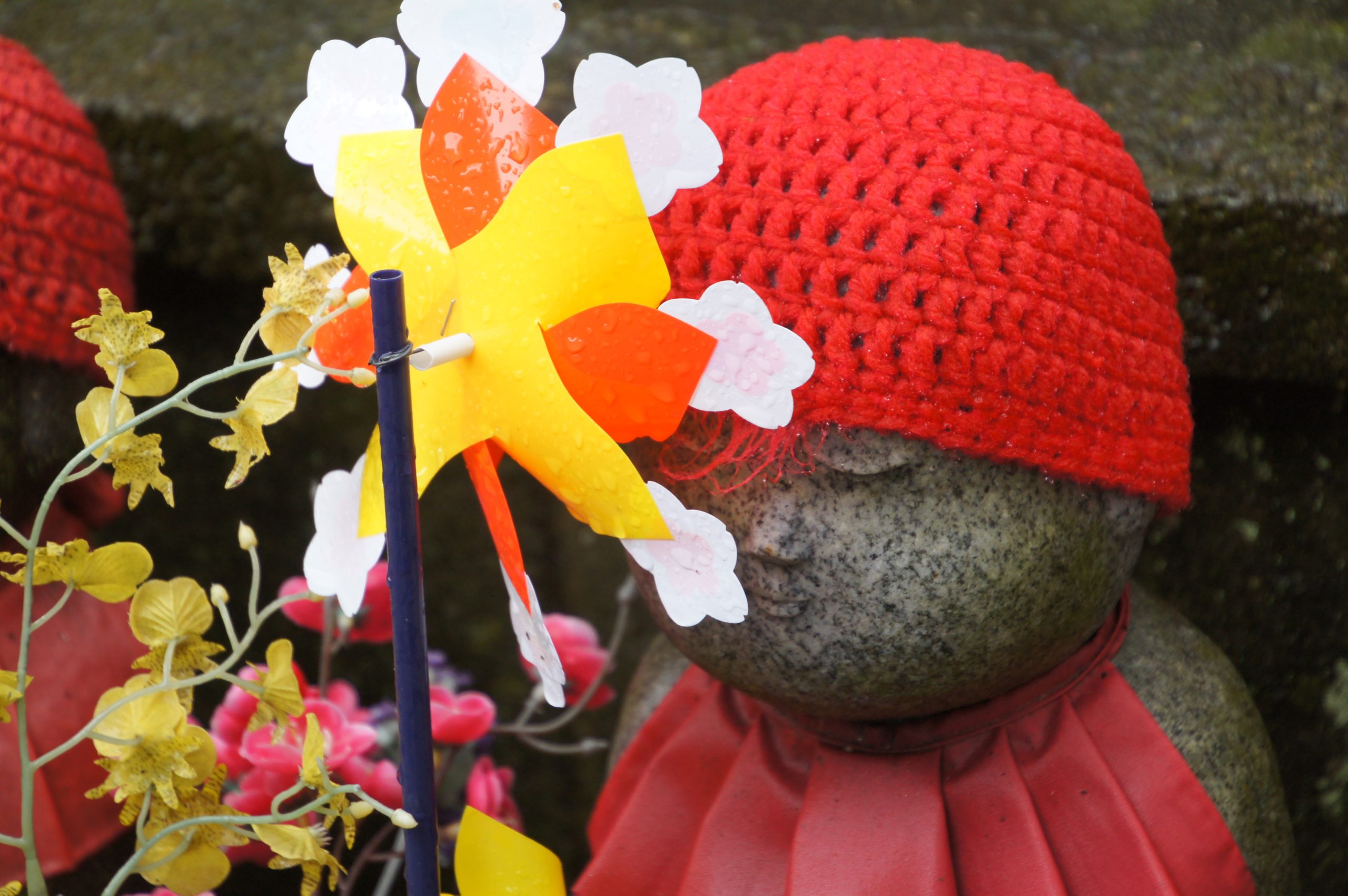 DSC07136 scaled A Jizo statue wearing a red knitted cap beside colourful pinwheels at Zojoji