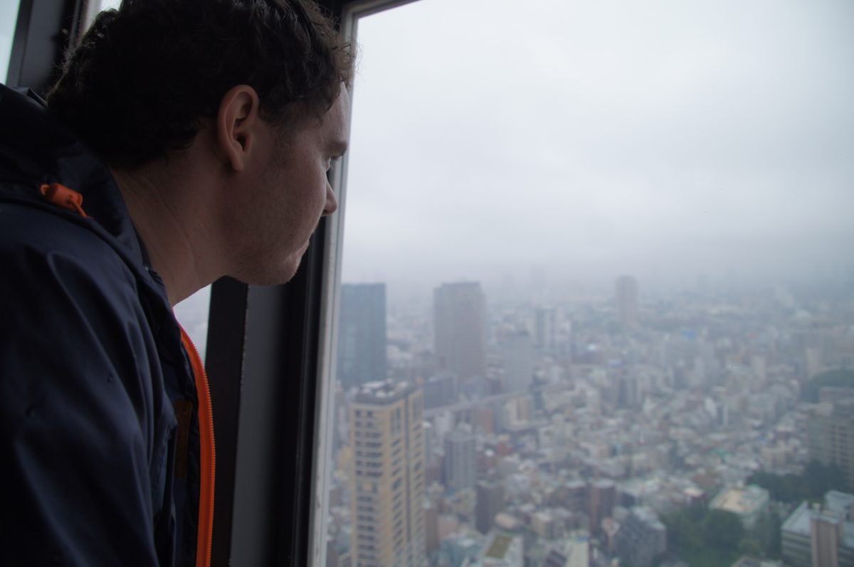DSC07196 A man in a dark jacket looking through a Tokyo Tower window towards the hazy city.