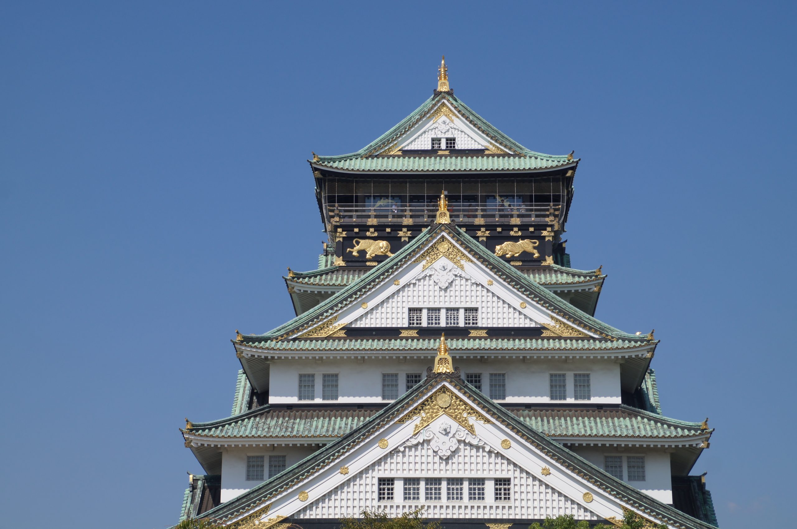 Osaka Castle's white walls, green roofs and gold decoration against a clear blue sky