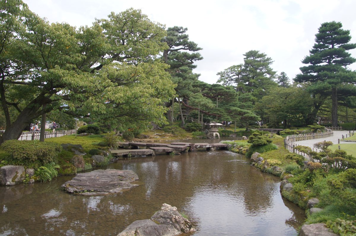 Shallow stream, stone bridges and clipped trees in Kenroku-en Garden
