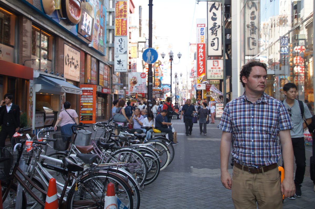 Gary walking through a busy Dotonbori street beside parked bicycles and restaurant signs