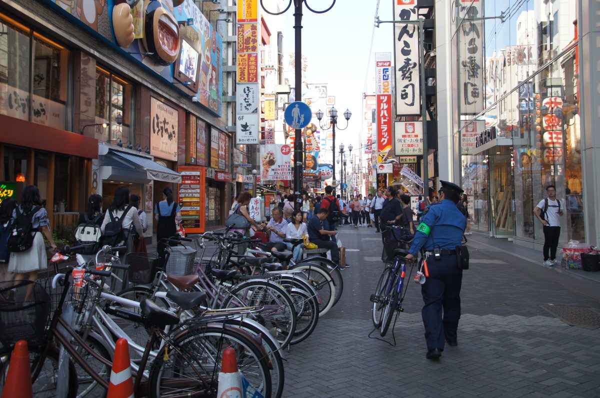 Crowded daytime street in Dotonbori lined with restaurants and colourful signs