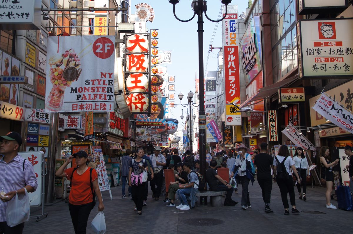 Dense restaurant signs along a Dotonbori street under a clear blue sky