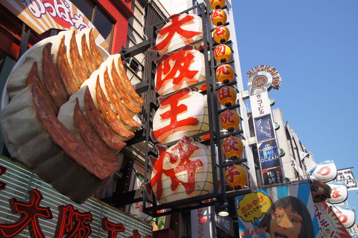 Oversized gyoza restaurant sign and lanterns against a blue sky in Dotonbori