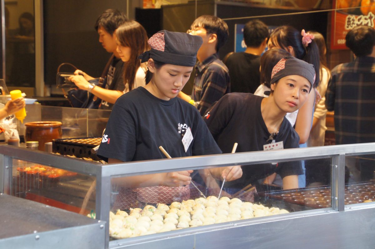 Cooks preparing takoyaki behind a busy Dotonbori counter