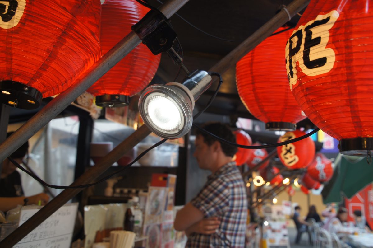 Red lanterns above a Dotonbori food counter with Gary standing beside it