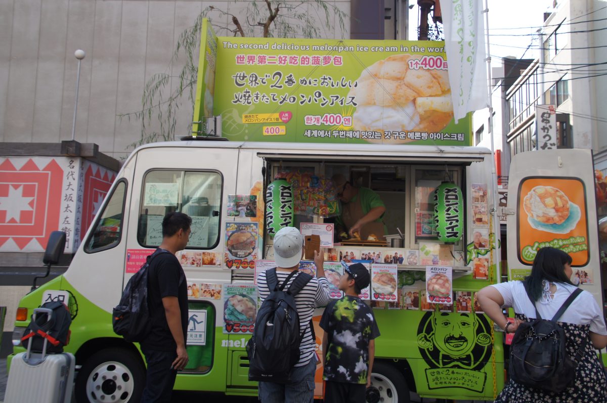 Customers ordering melonpan ice cream from a green food van in Dotonbori
