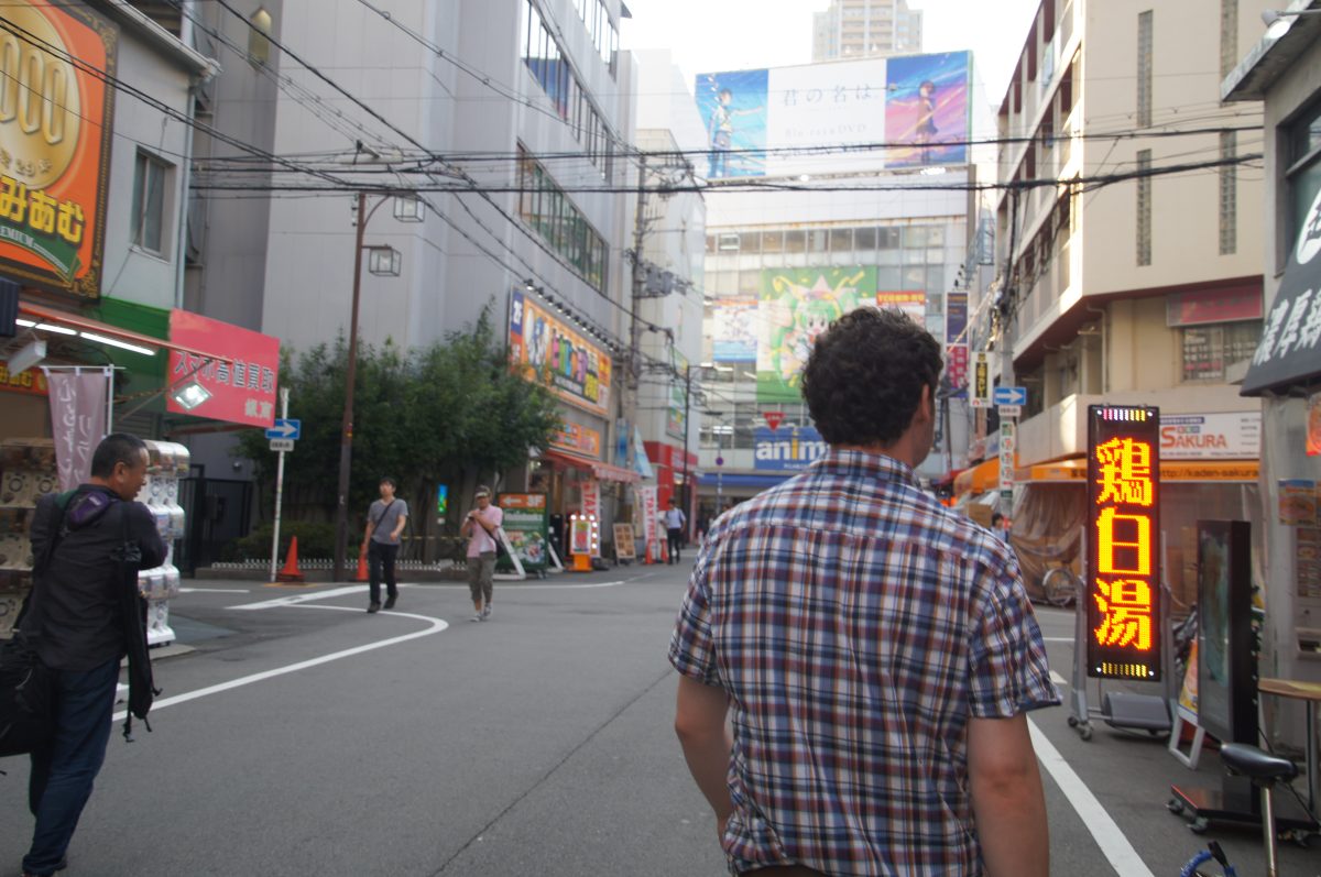Pedestrians walking beneath shop signs in Den Den Town, Osaka