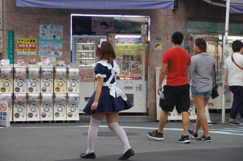 DSC09800 2 Maid promoter walking past capsule-toy machines in Den Den Town, Osaka