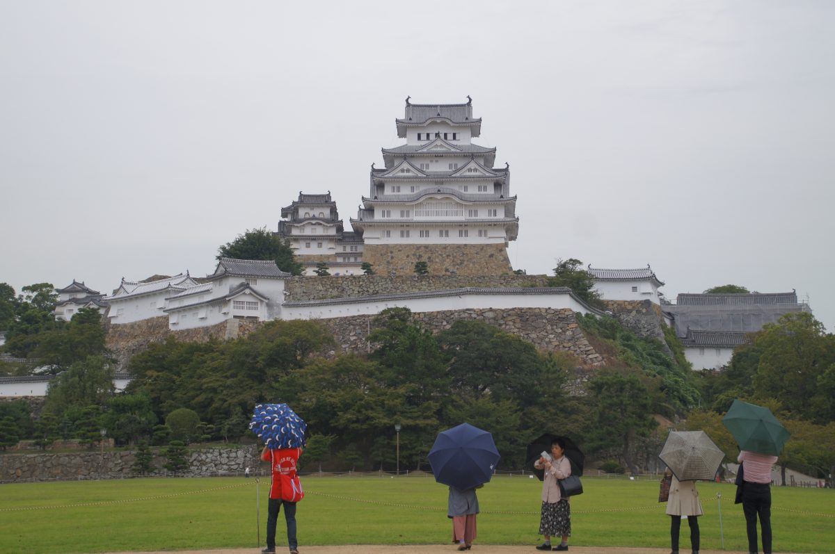 Himeji Castle seen across the lawn with visitors holding umbrellas