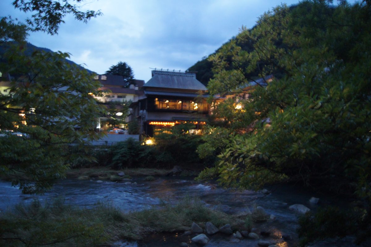 Hakone 104 A river and lit inns among trees at dusk in Hakone.