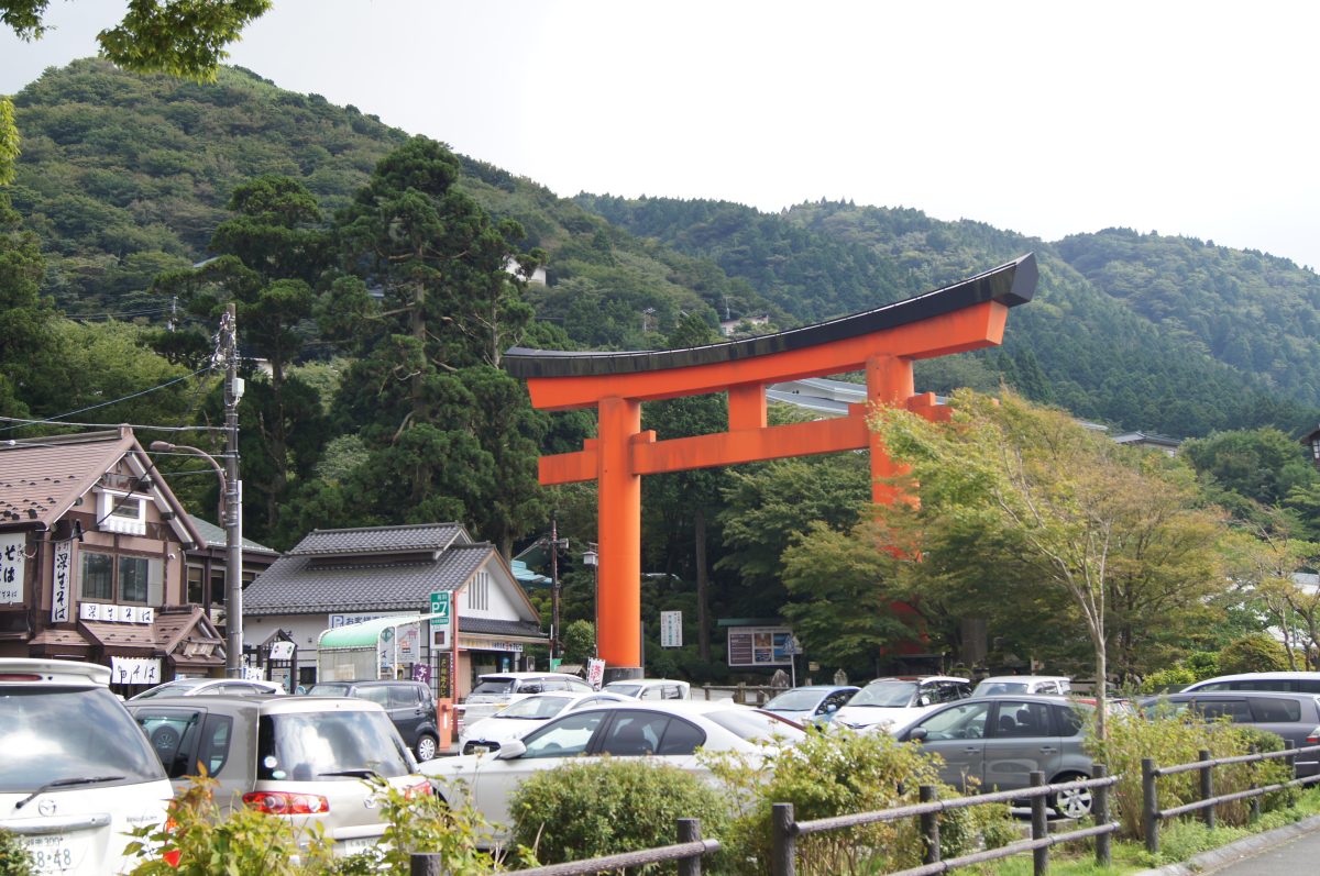 Hakone 5 A red torii gate above a small car park with forested hills behind it in Hakone.