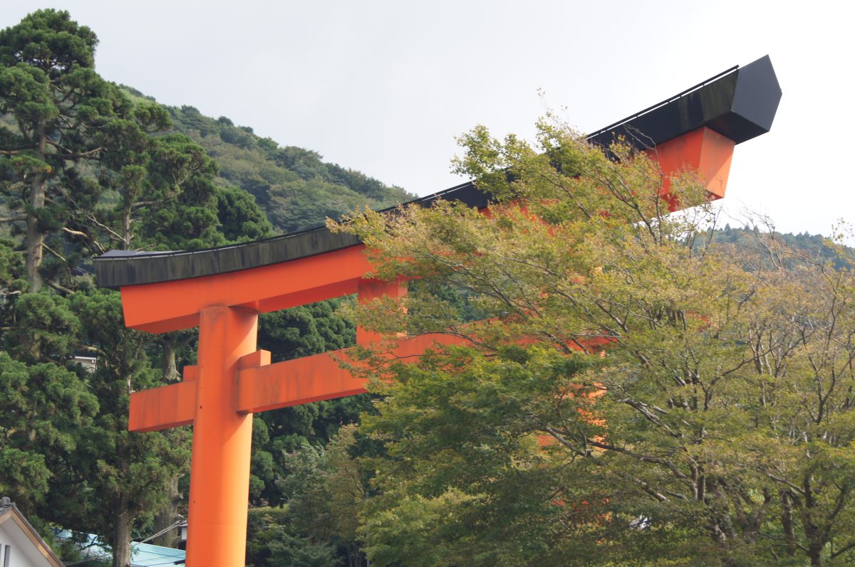 Hakone 6 A red torii gate framed by leaves against a cloudy sky in Hakone.