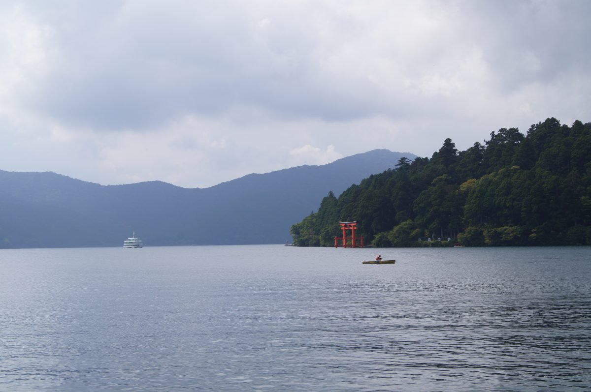 Hakone 8 Lake Ashi with a red torii gate standing in the water at the edge of the forest.