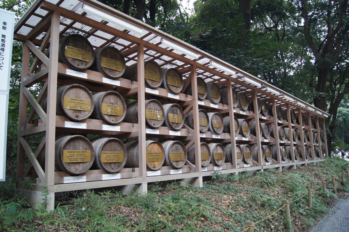 Rows of barrels on a wooden rack among trees at Meiji Jingu.