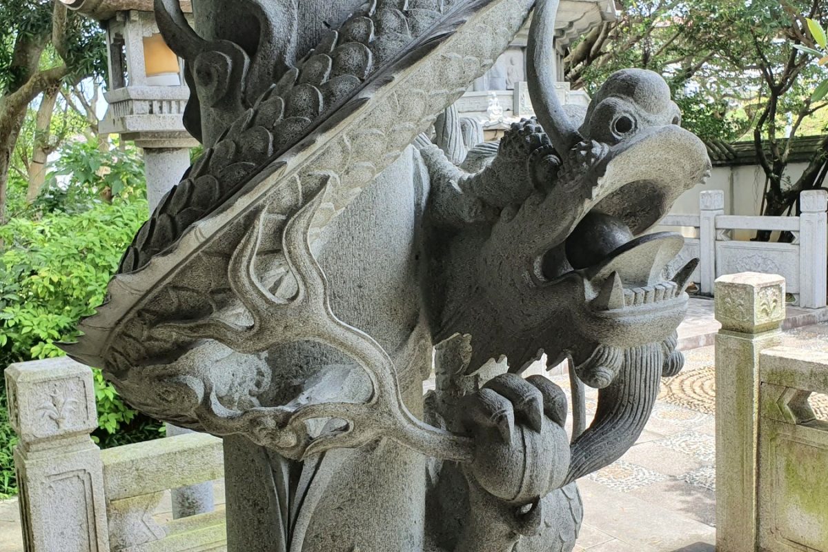 Ornate stone carving in Okinawa Close-up of an ornate stone carving surrounded by trees and stone balustrades.