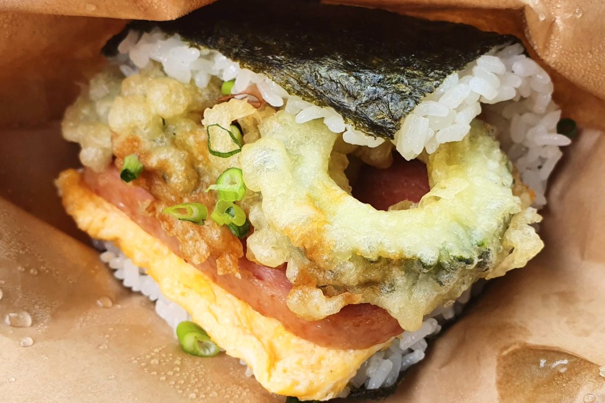 Close-up of a rice sandwich with bitter melon tempura, egg and pork inside a paper wrapper.