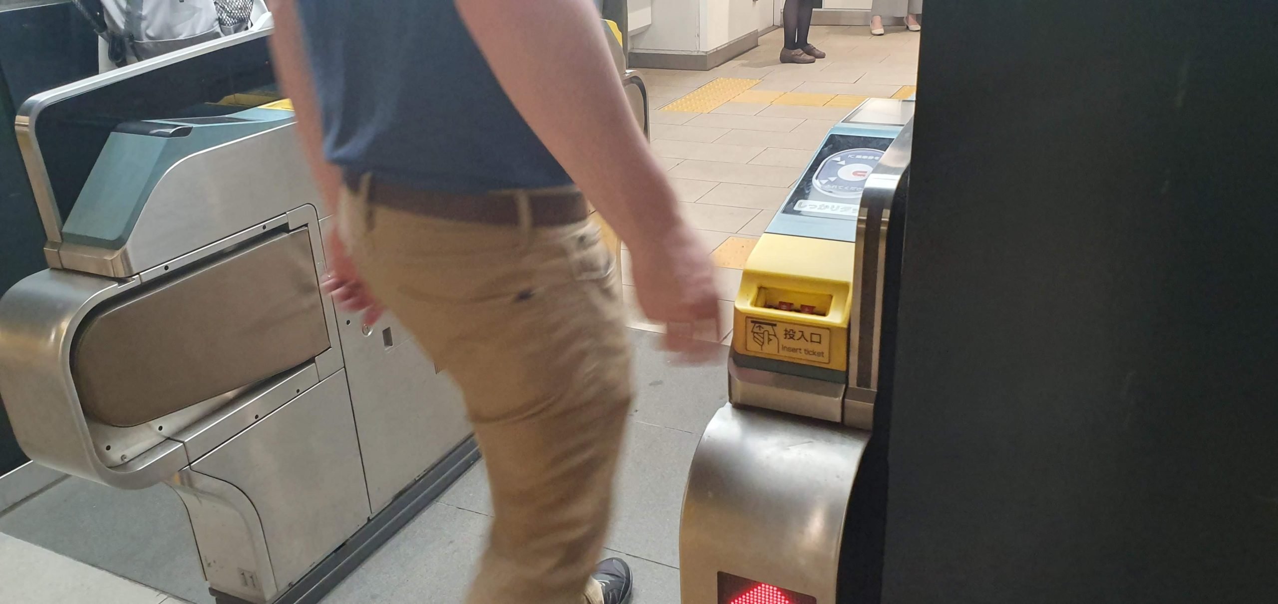 Shinjuku Station 13 scaled A traveller passes through a Japanese station ticket gate beside an IC-card reader and tactile paving.