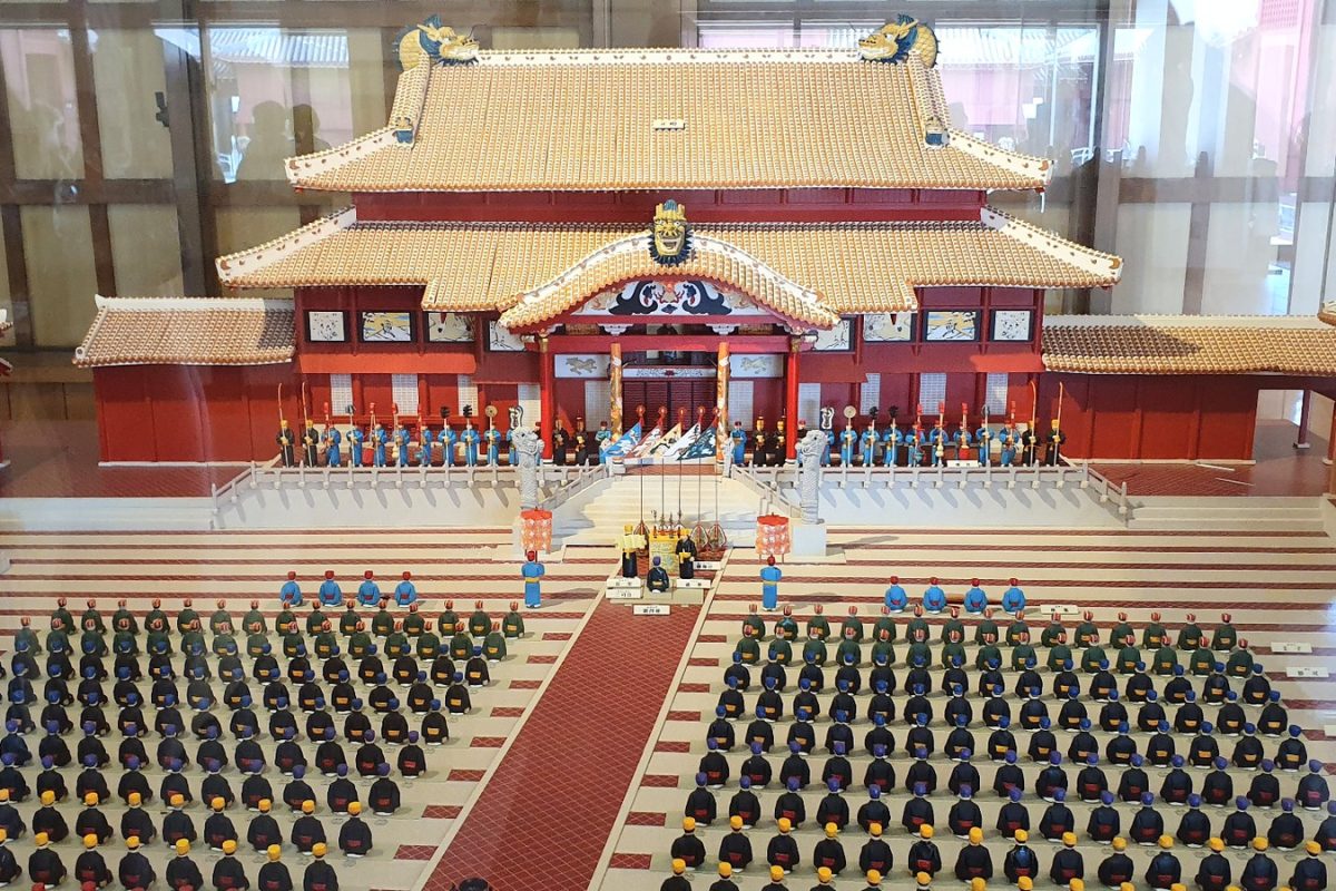 Model of Shuri Castle with rows of figures arranged around a red path in the courtyard.