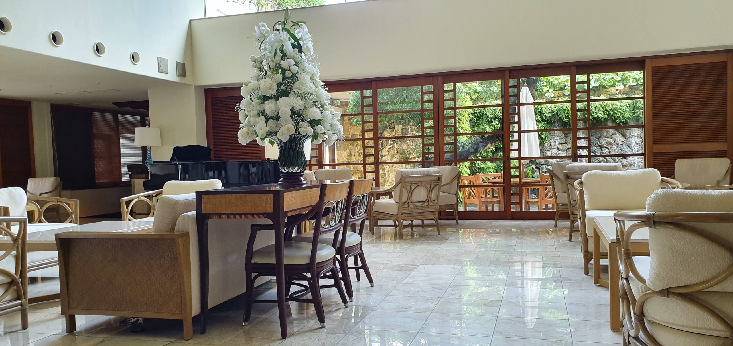 Armchairs, tables and a large flower arrangement furnish the bright lobby lounge at The Naha Terrace in Okinawa.