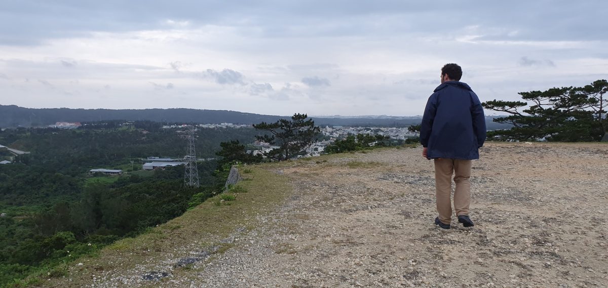 A visitor stands on the elevated castle ruins overlooking Yomitan and the Okinawan coast.