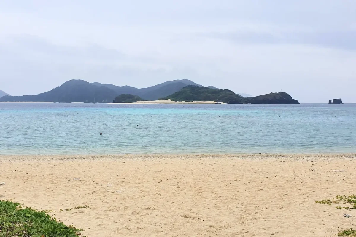 Sand and turquoise water at Ama Beach beneath an overcast sky