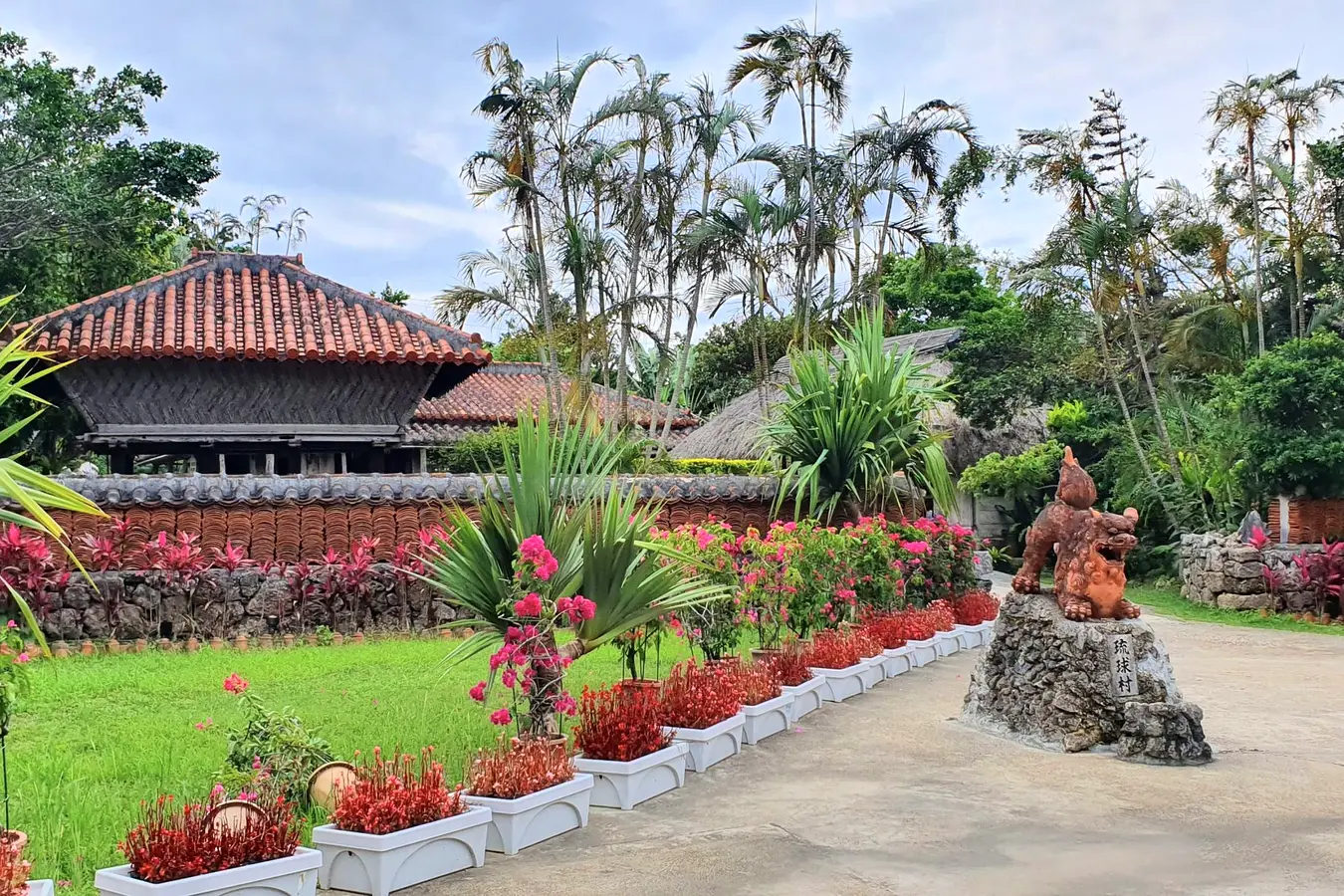 Red tiled gateway surrounded by palms and flowers at Ryukyu Mura