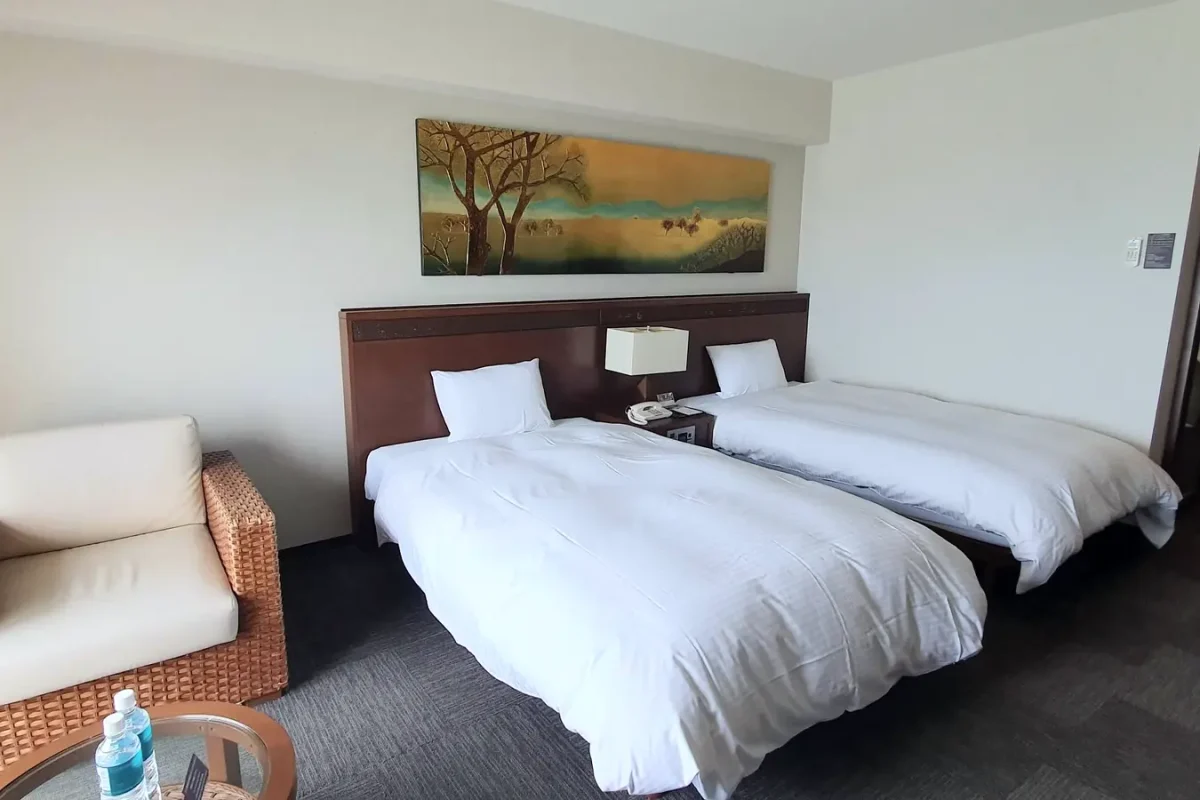 Twin beds and a wicker armchair in our room at Grandvrio Resort Ishigakijima