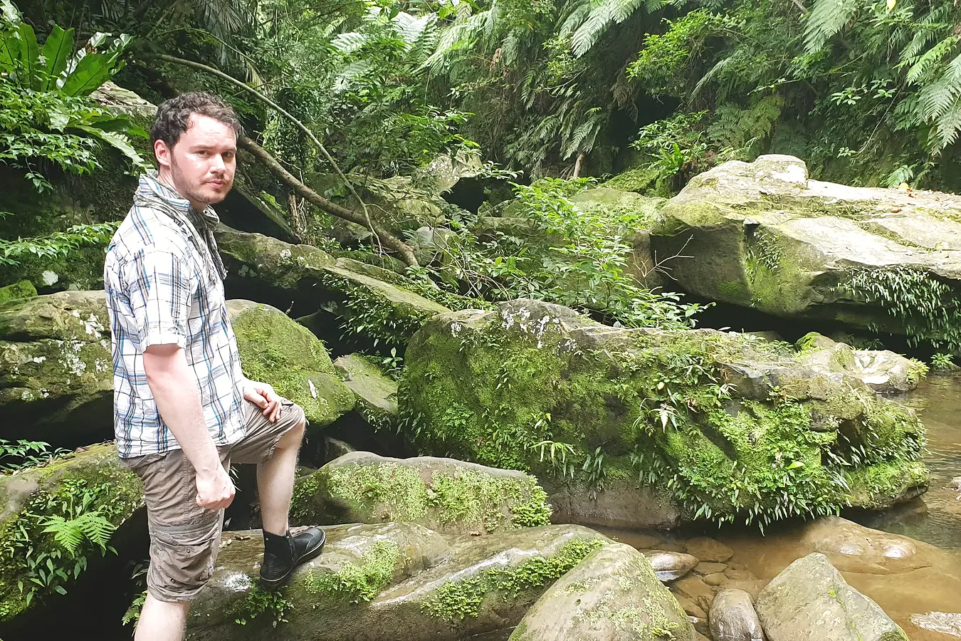 Gary beside moss-covered rocks and a forest stream on Iriomote